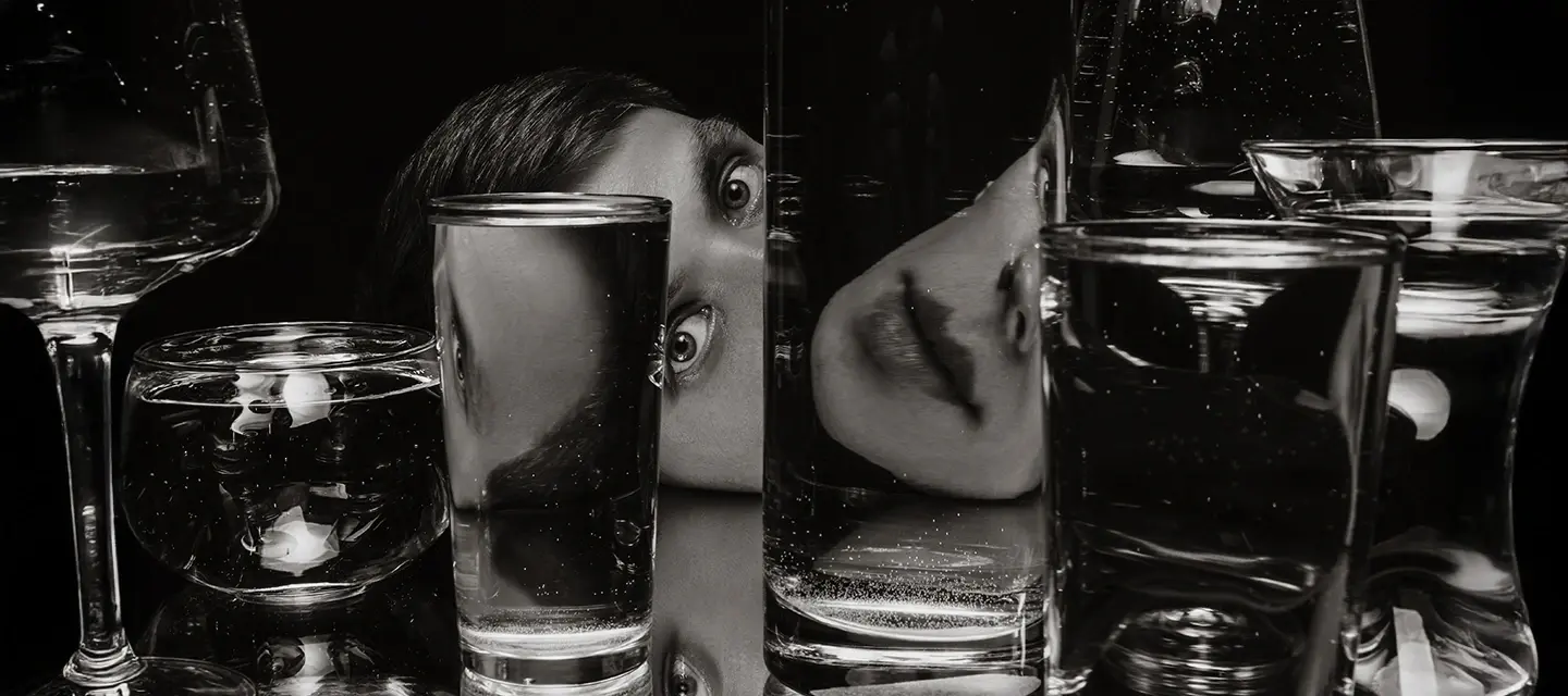 A person with interesting eyes with a face deconstructed by glasses of water in front of them
